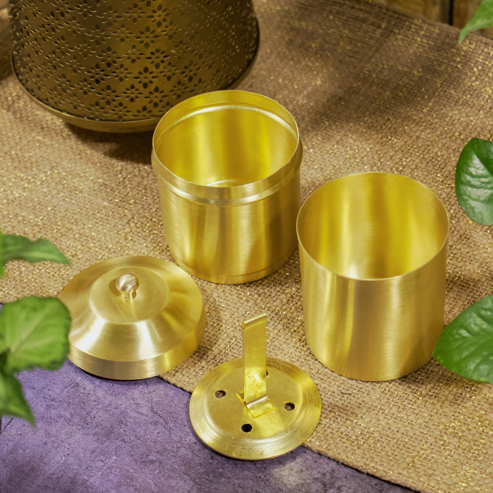 Set of gold metal containers and lids on a textured surface with leaves.
