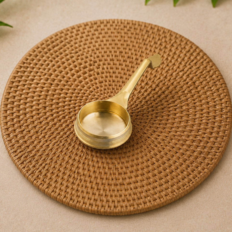 A brass ladle with a polished gold finish rests on a round woven brown placemat over a beige textured surface.
