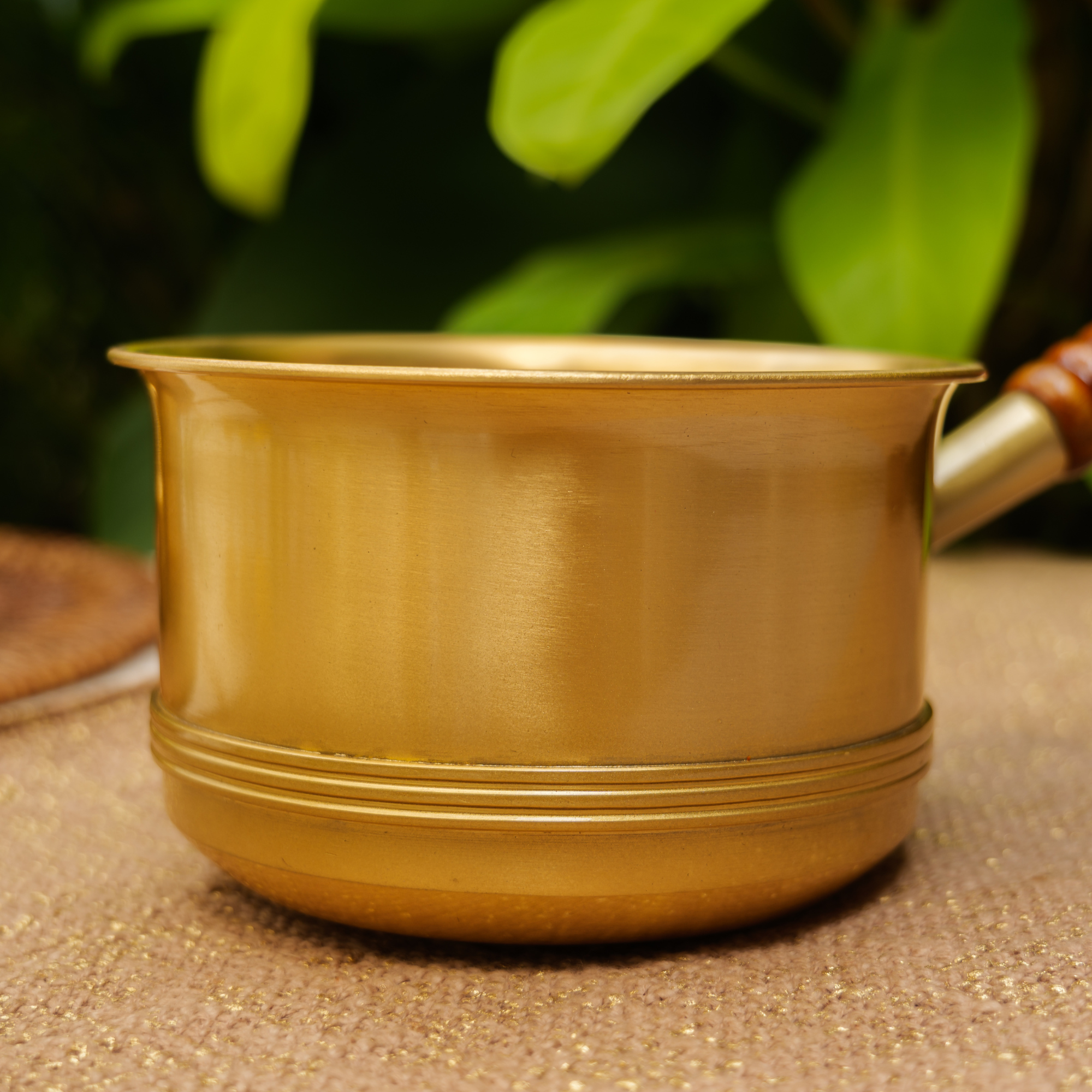 Gold pot on a textured surface with blurred green leaves in the background