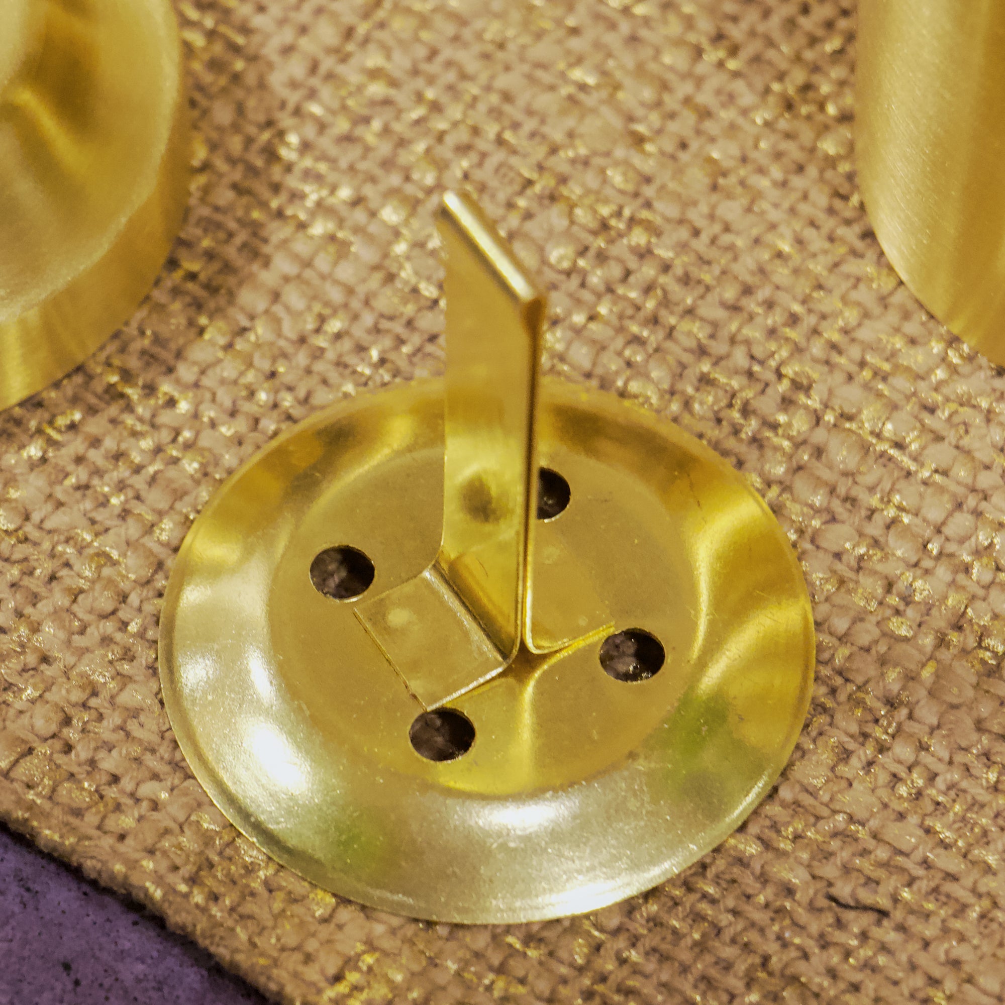 Gold circular object with a central spike on a textured beige surface