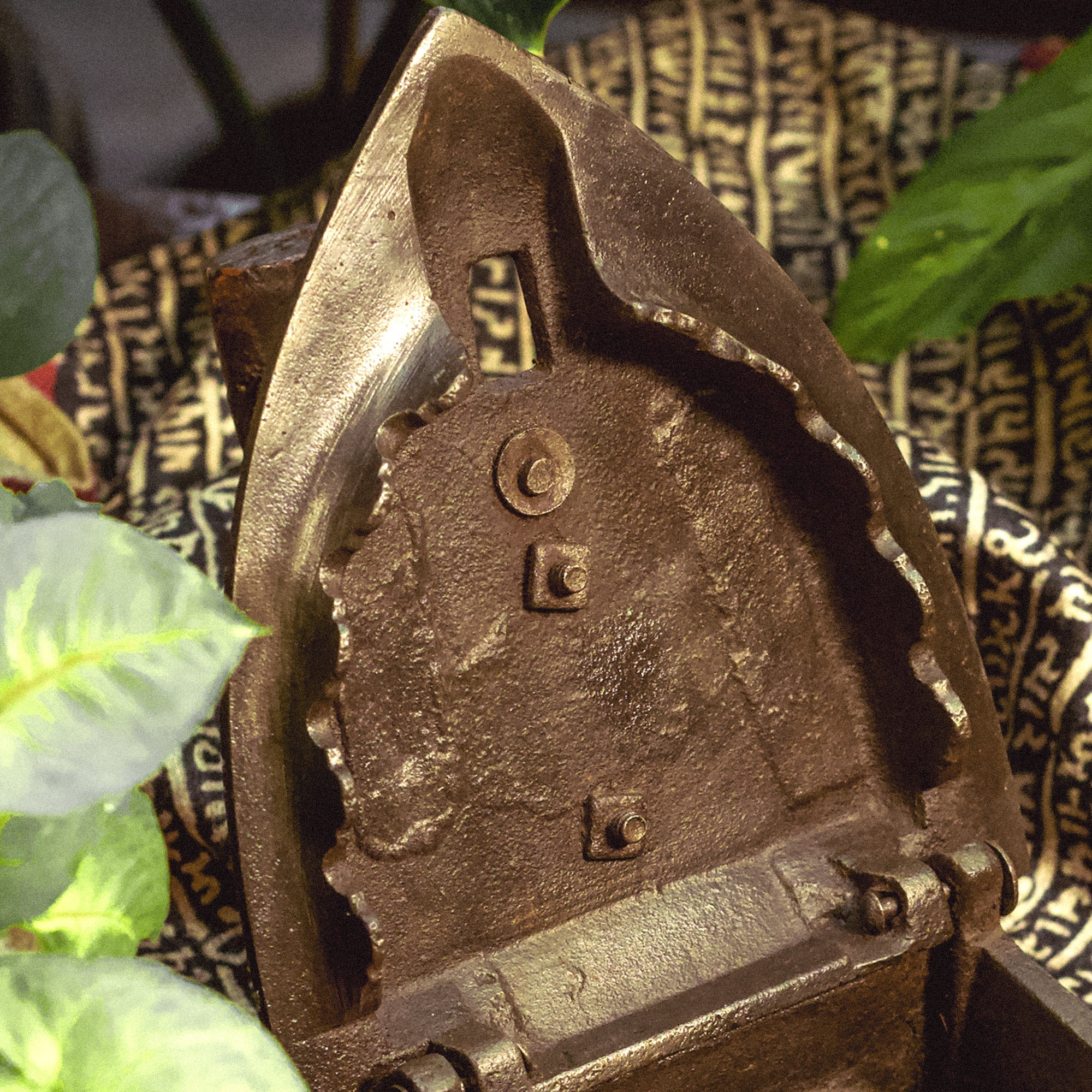 Bronze or brown metal object with intricate details against a patterned fabric background