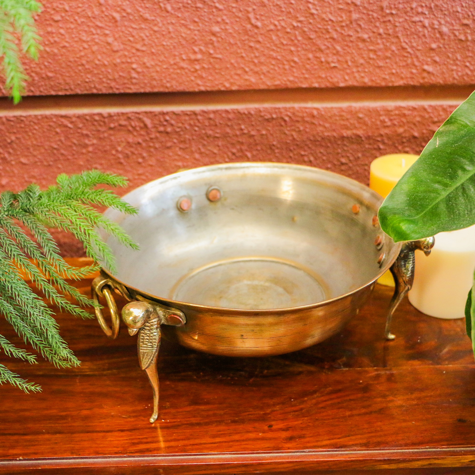 Decorative metal bowl with fairy design on a wooden surface with plants and candles.