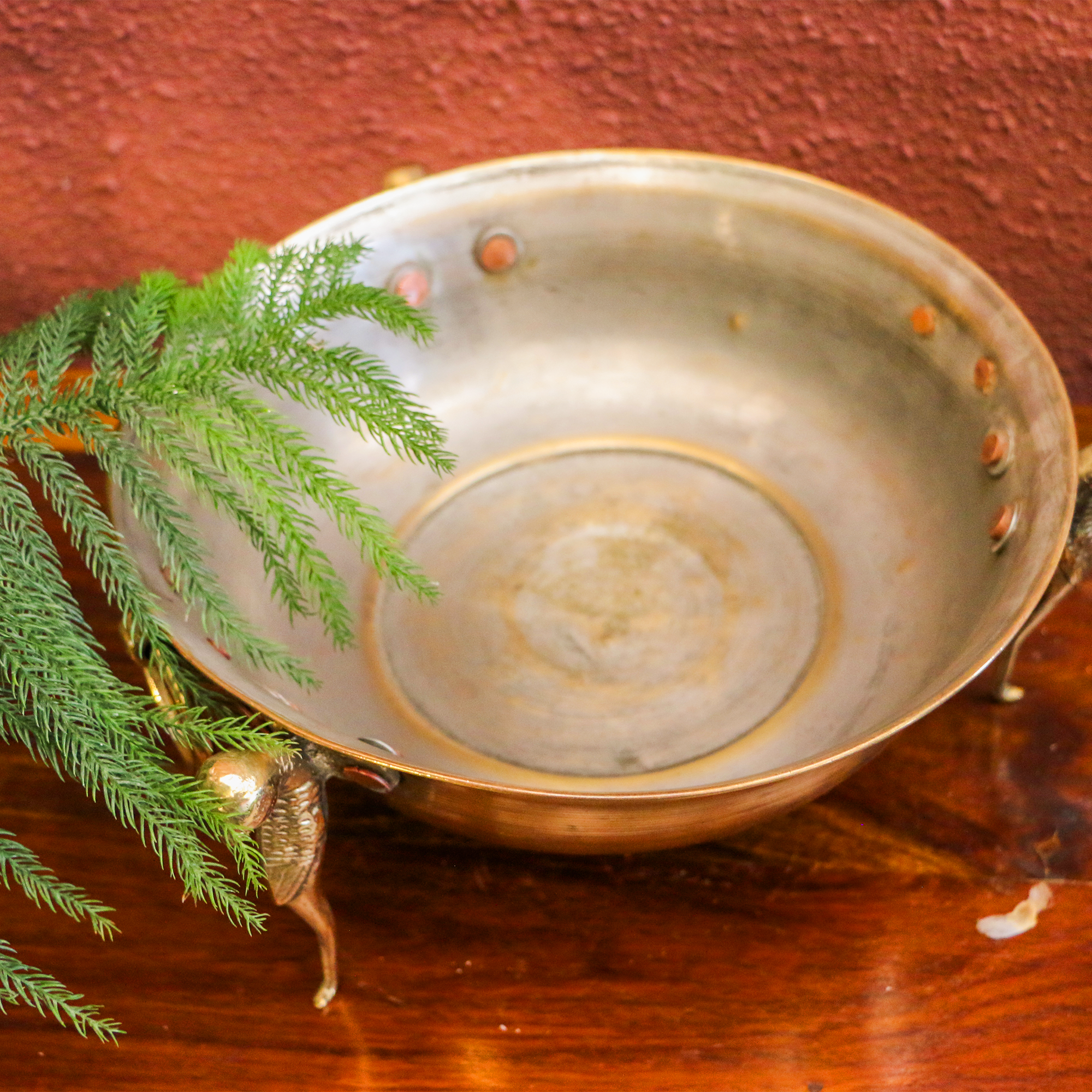Decorative metal bowl with greenery on a wooden surface