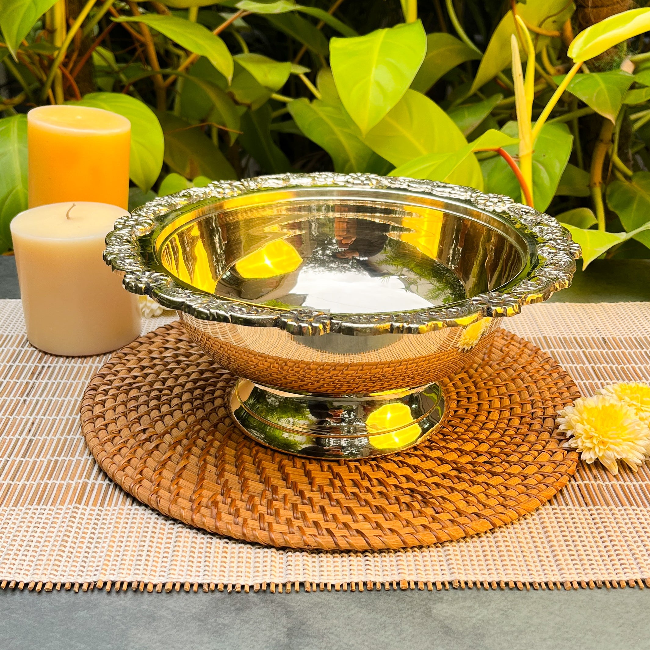 Decorative silver bowl on a woven mat with candles and flowers in the background