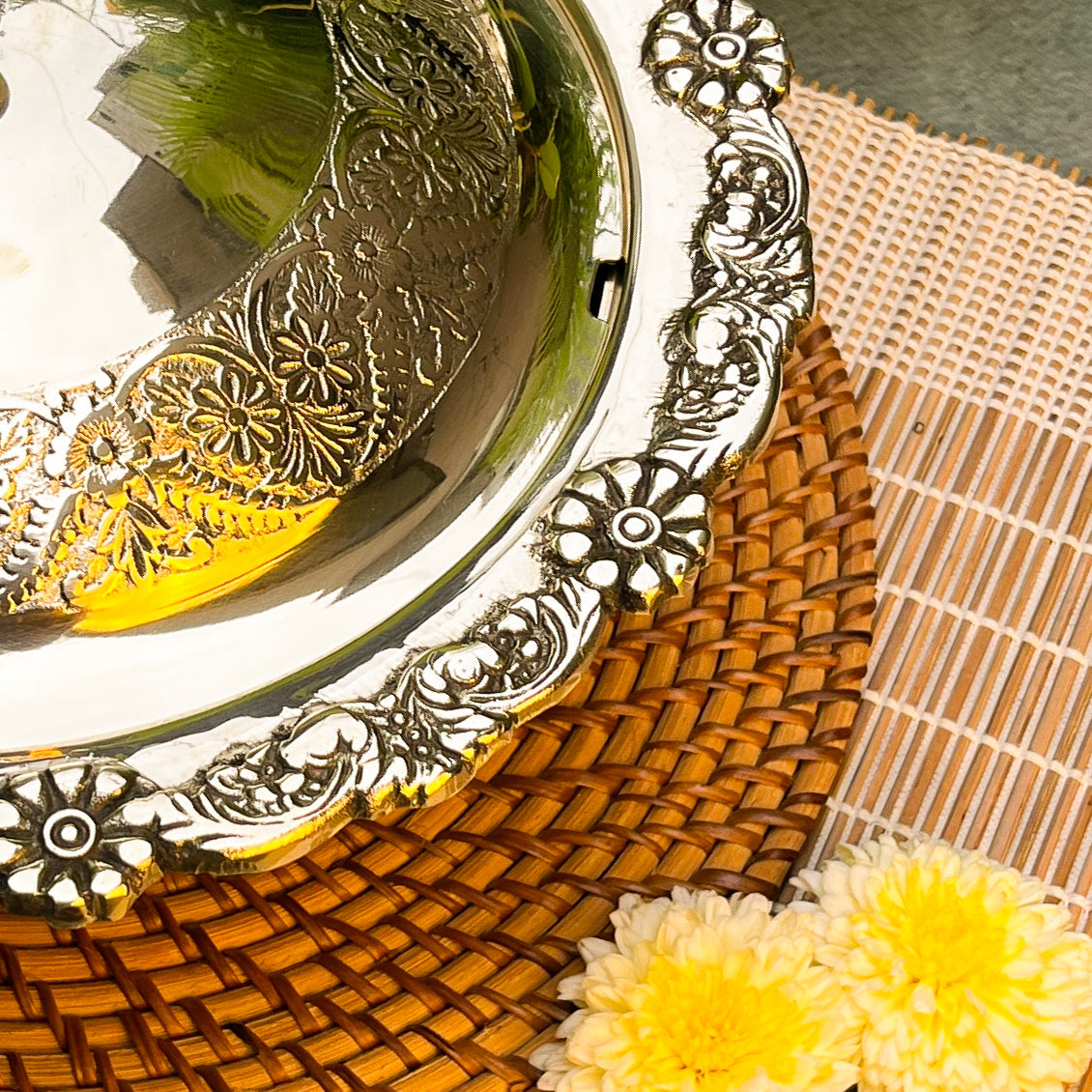Decorative silver plate with intricate designs on a woven mat with yellow flowers.