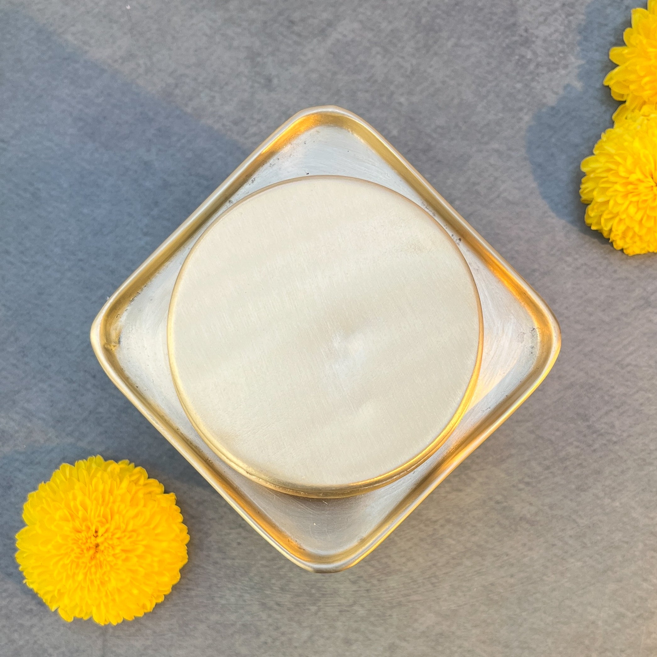 Round white object in a gold frame on a gray surface with yellow flowers