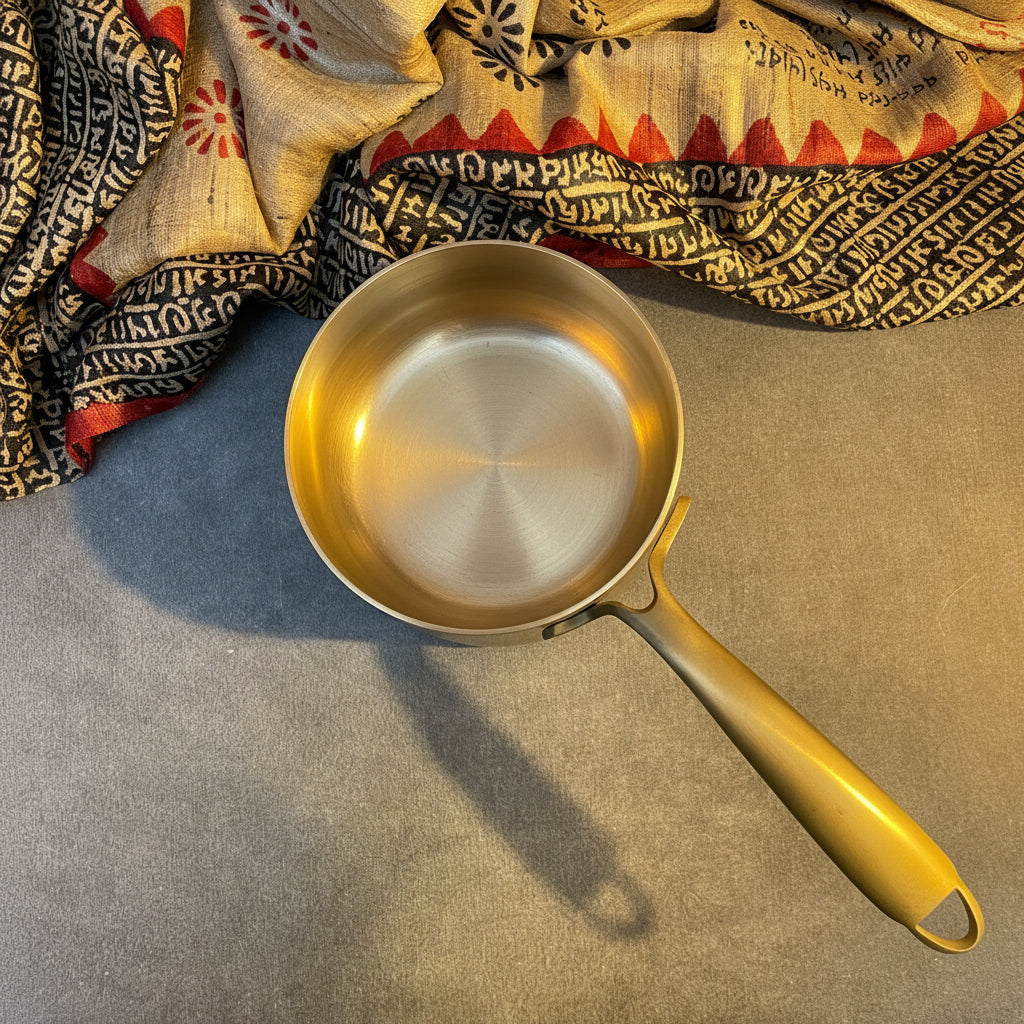 Silver saucepan with yellow handle on a textured surface with patterned fabric in the background