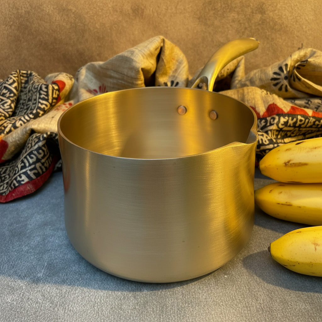 Stainless steel pot on a textured surface with bananas and fabric in the background