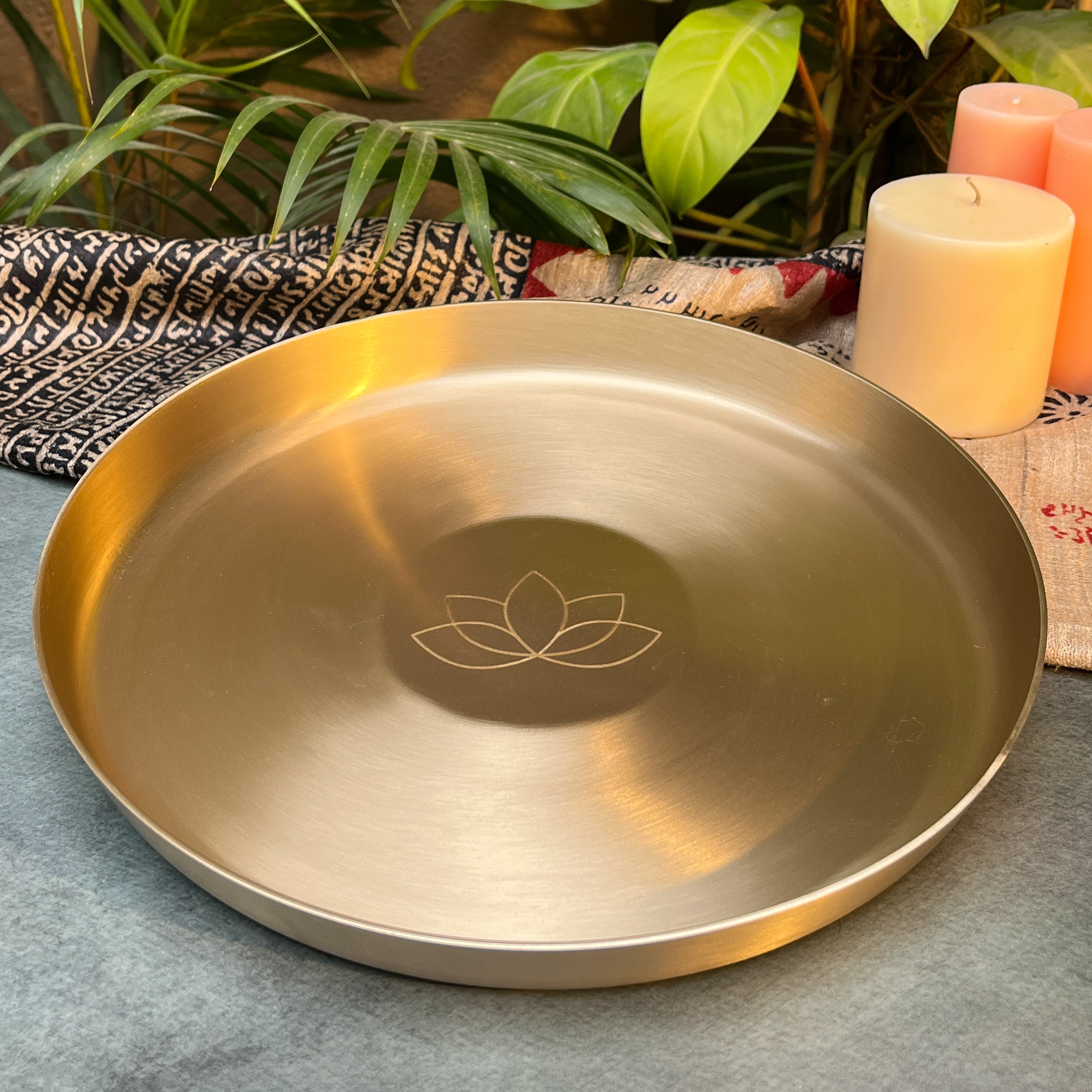Gold tray with 'Ambi Home' text and logo on a textured surface with candles and plants in the background.