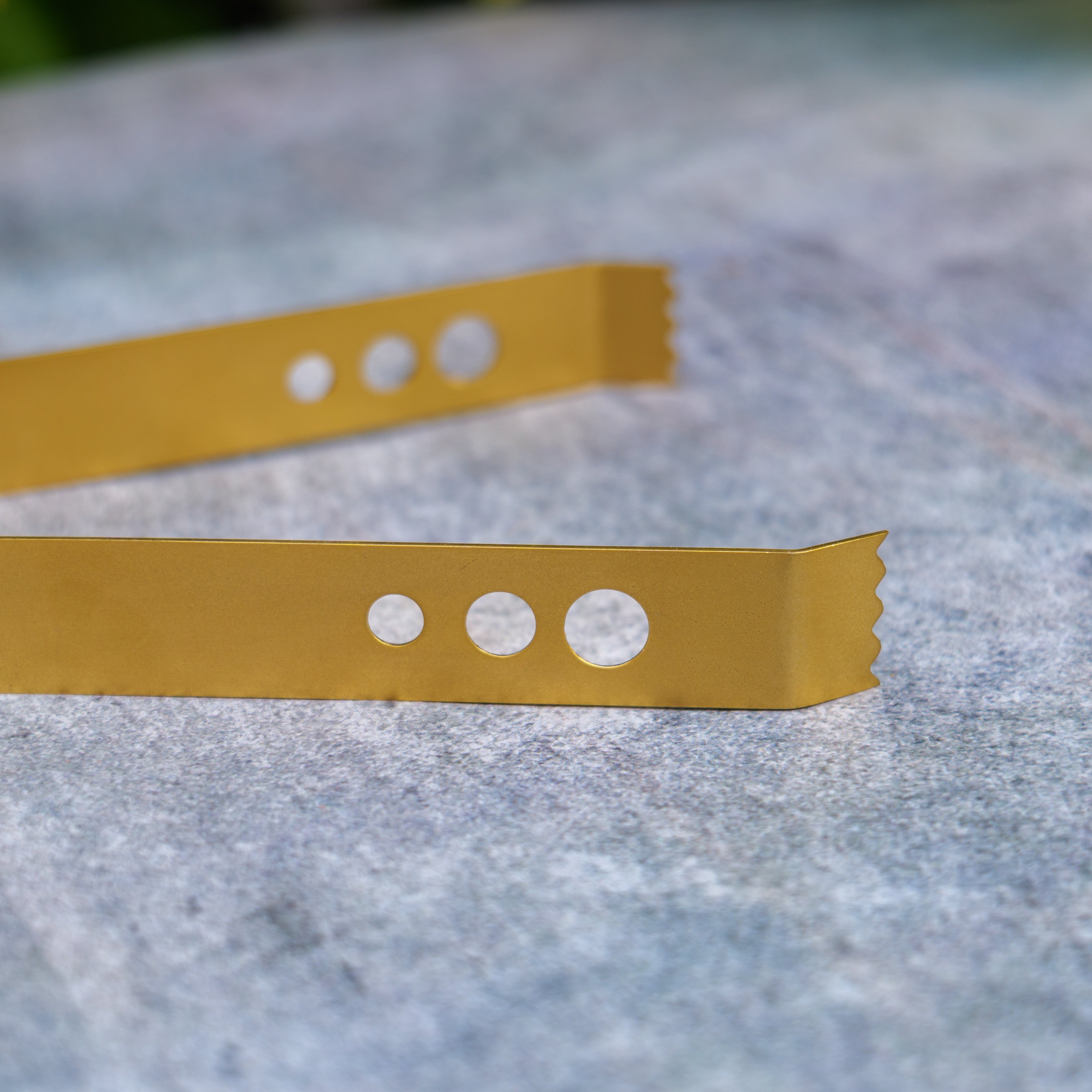 Two yellow metal strips with holes on a textured gray surface