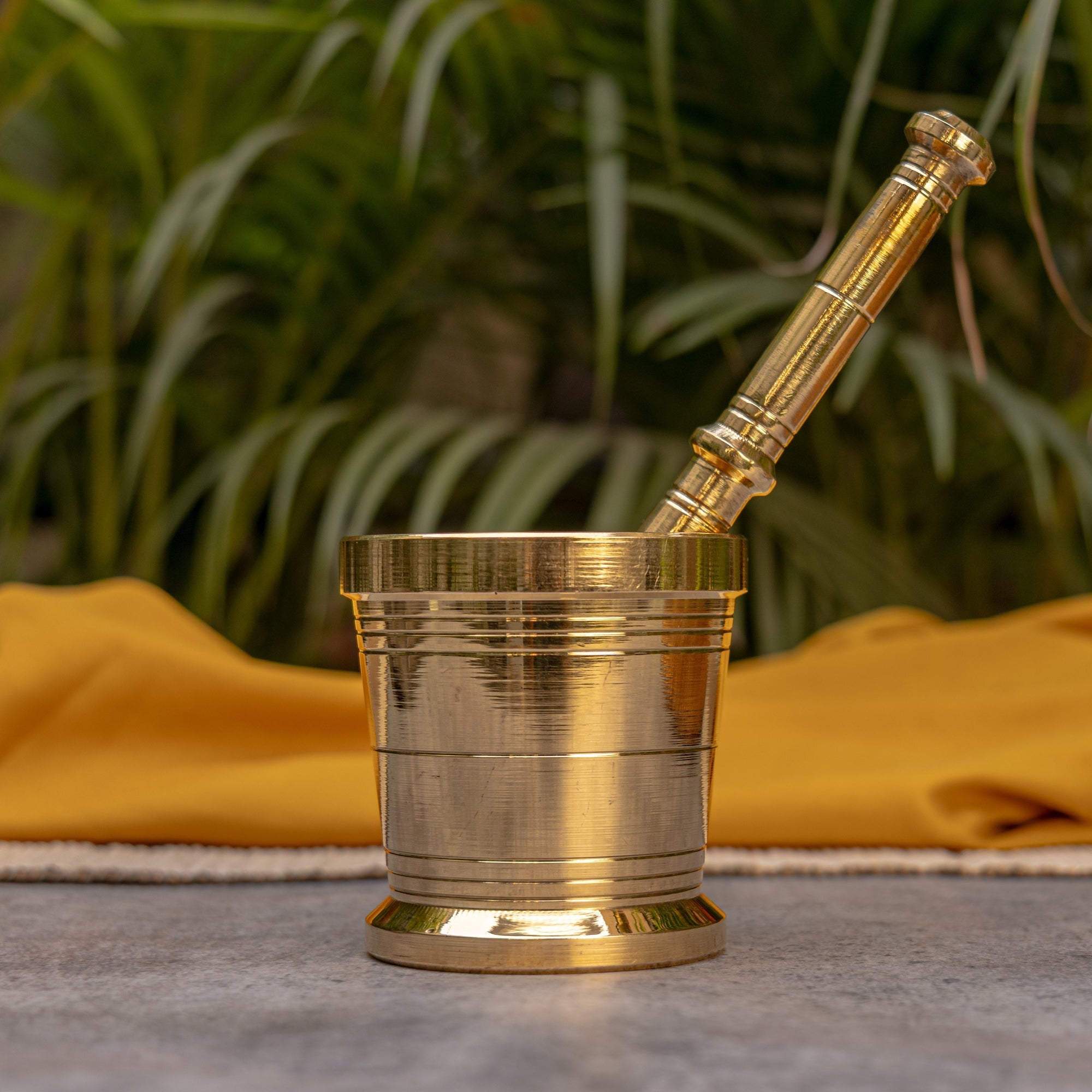 Brass mortar and pestle with 'ambi' branding on a yellow cloth with greenery in the background