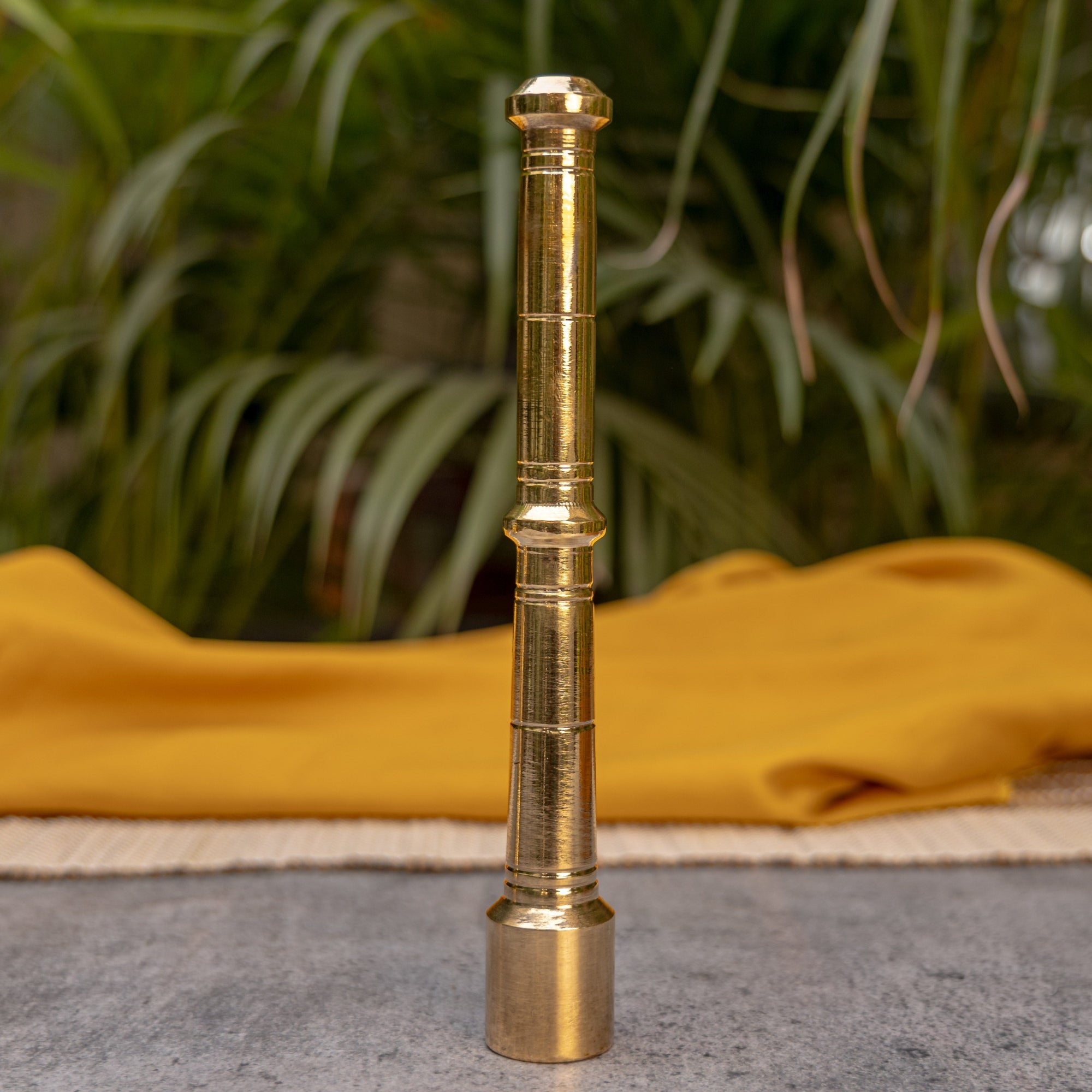 Gold-colored telescopic object on a textured surface with green foliage in the background