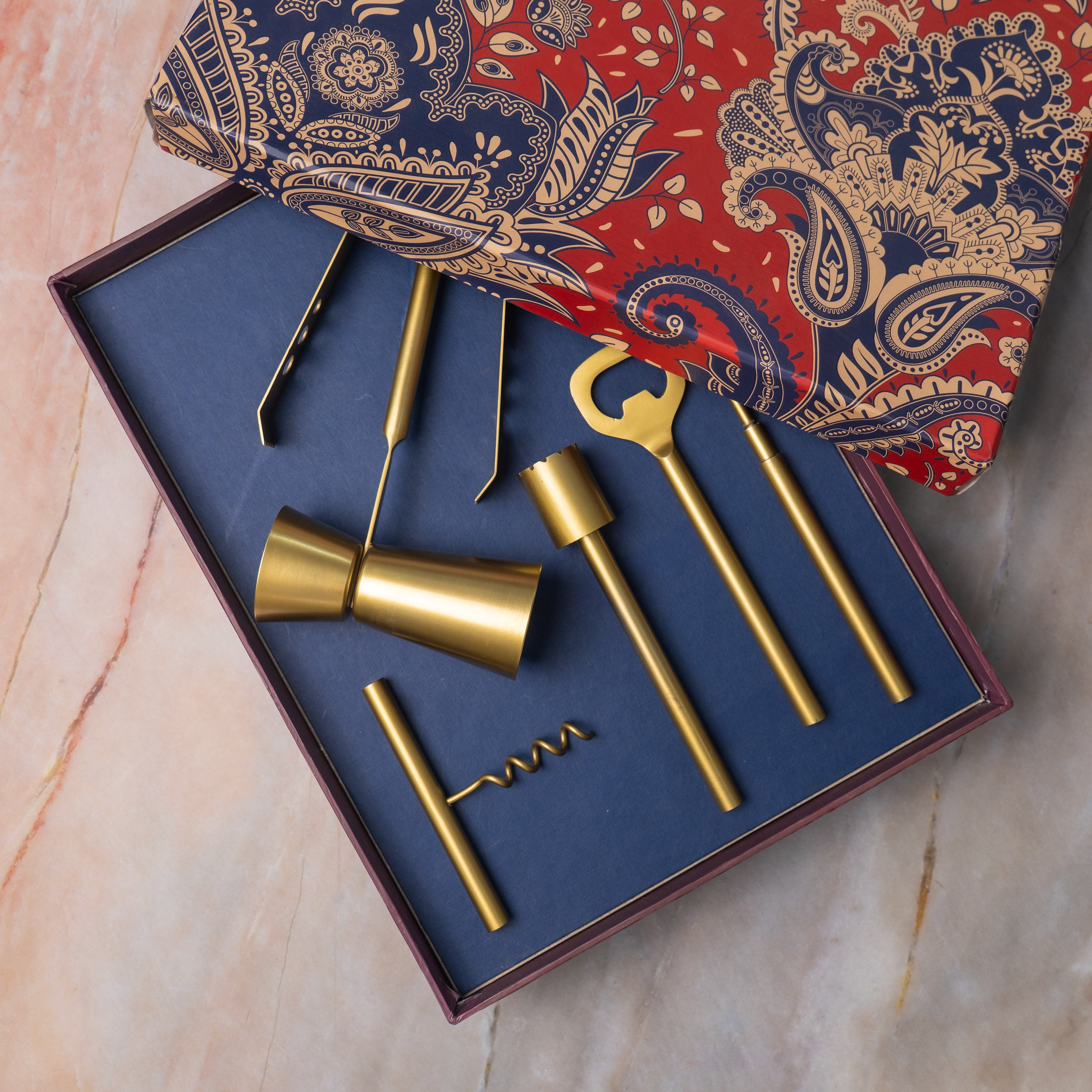 Set of gold bar tools including a jigger, strainer, and corkscrew in a decorative box with paisley design.