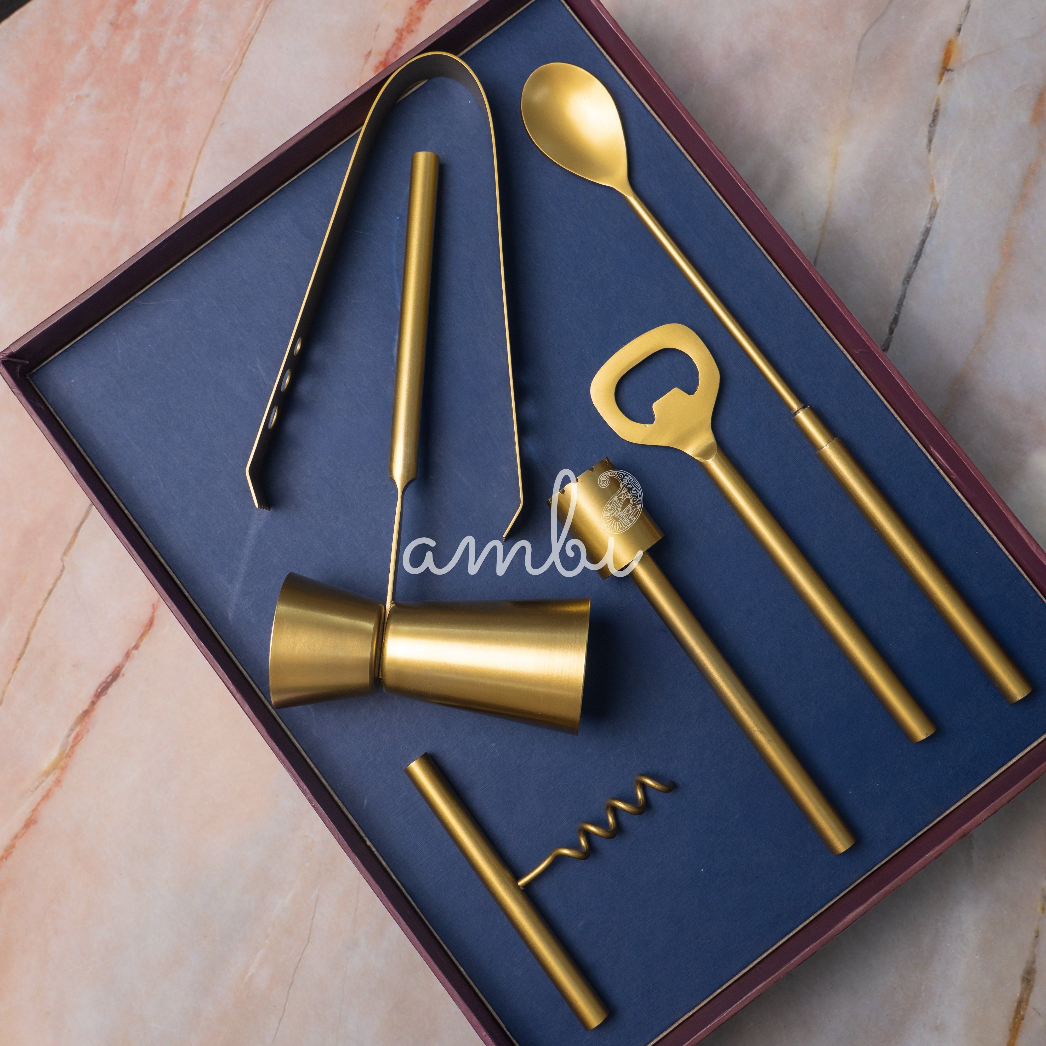 Set of gold bar tools including a jigger, bottle opener, and corkscrew on a blue background.