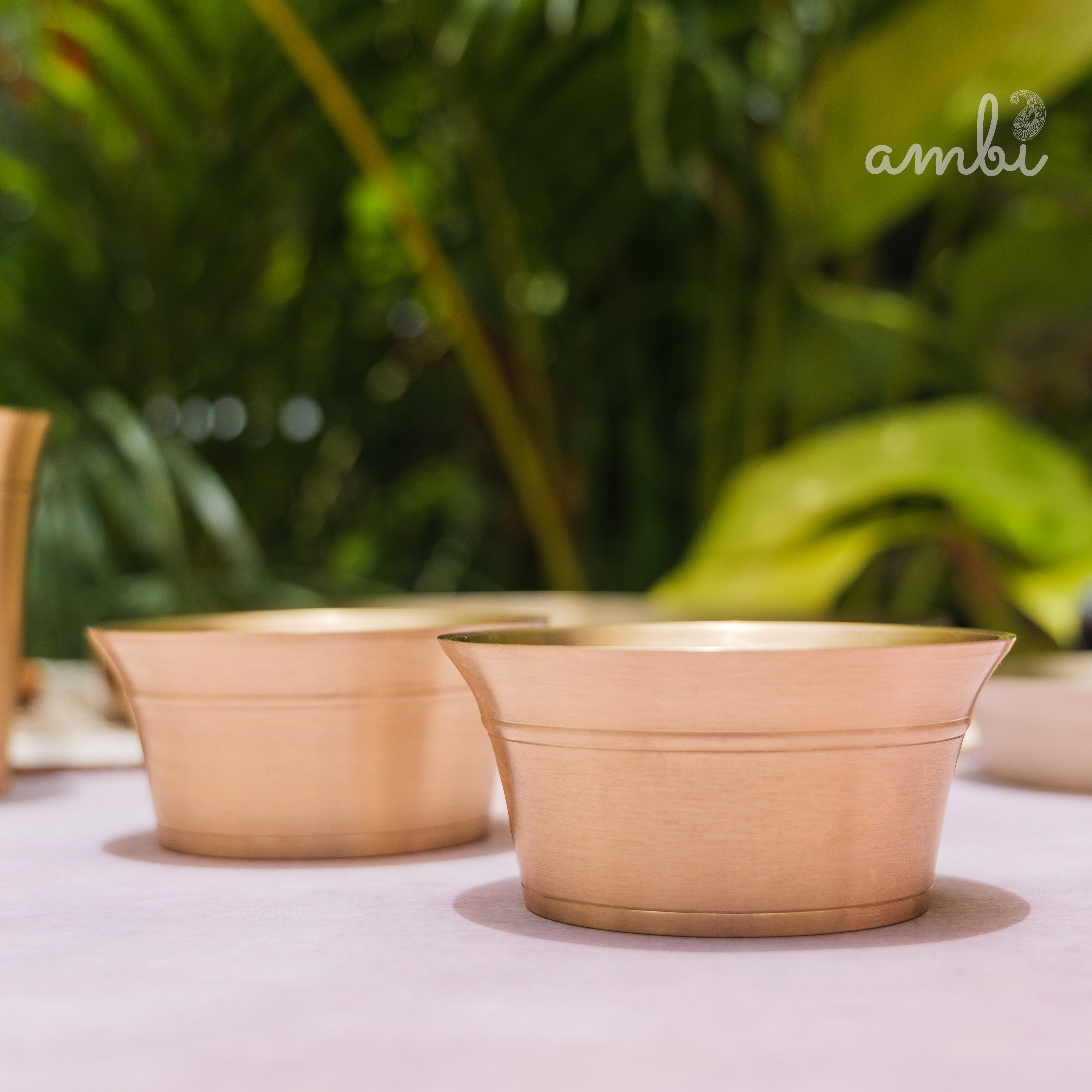 Two beige ceramic bowls on a pink surface with a blurred green plant background
