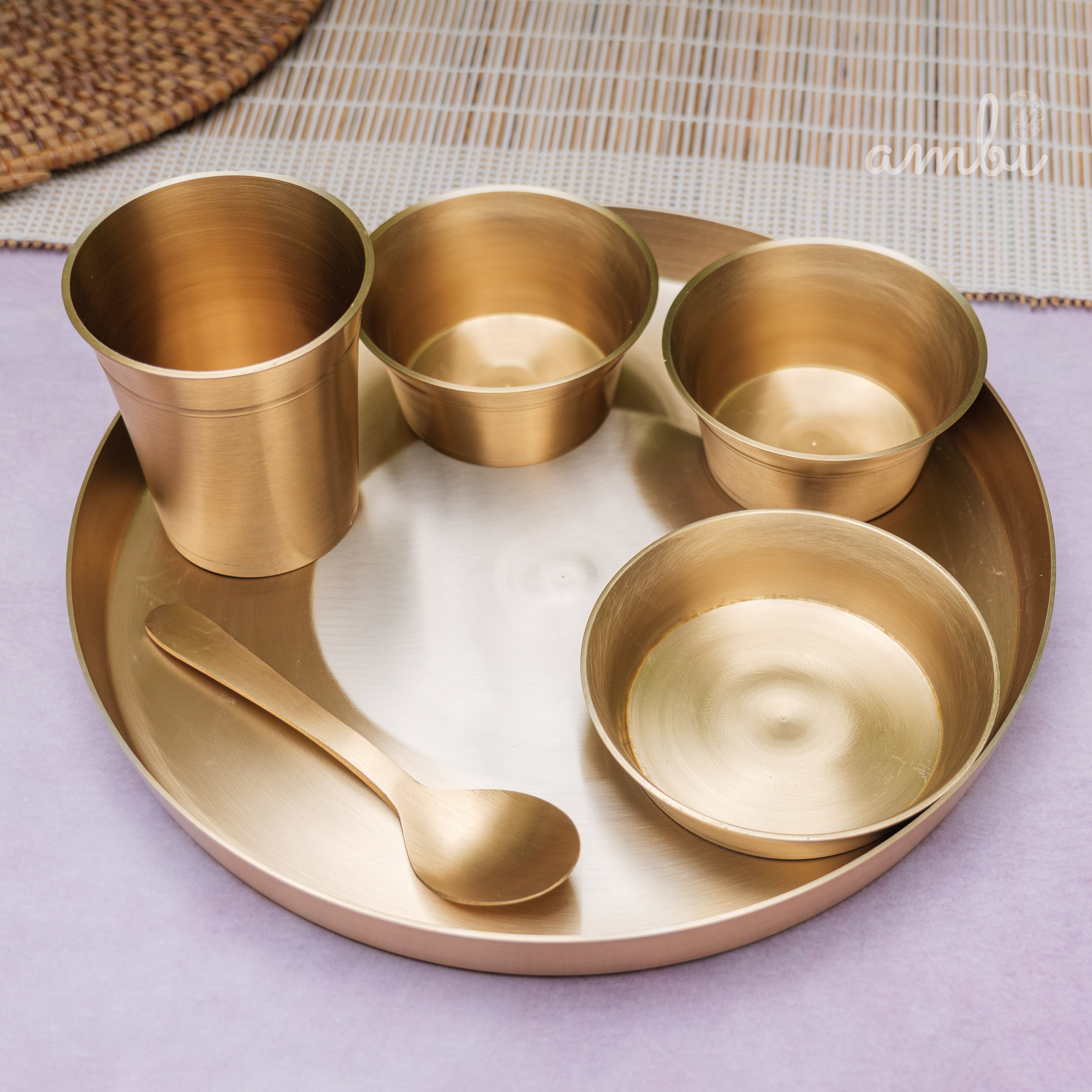 Set of gold-colored dining utensils including cups, bowls, and a spoon on a white tray.