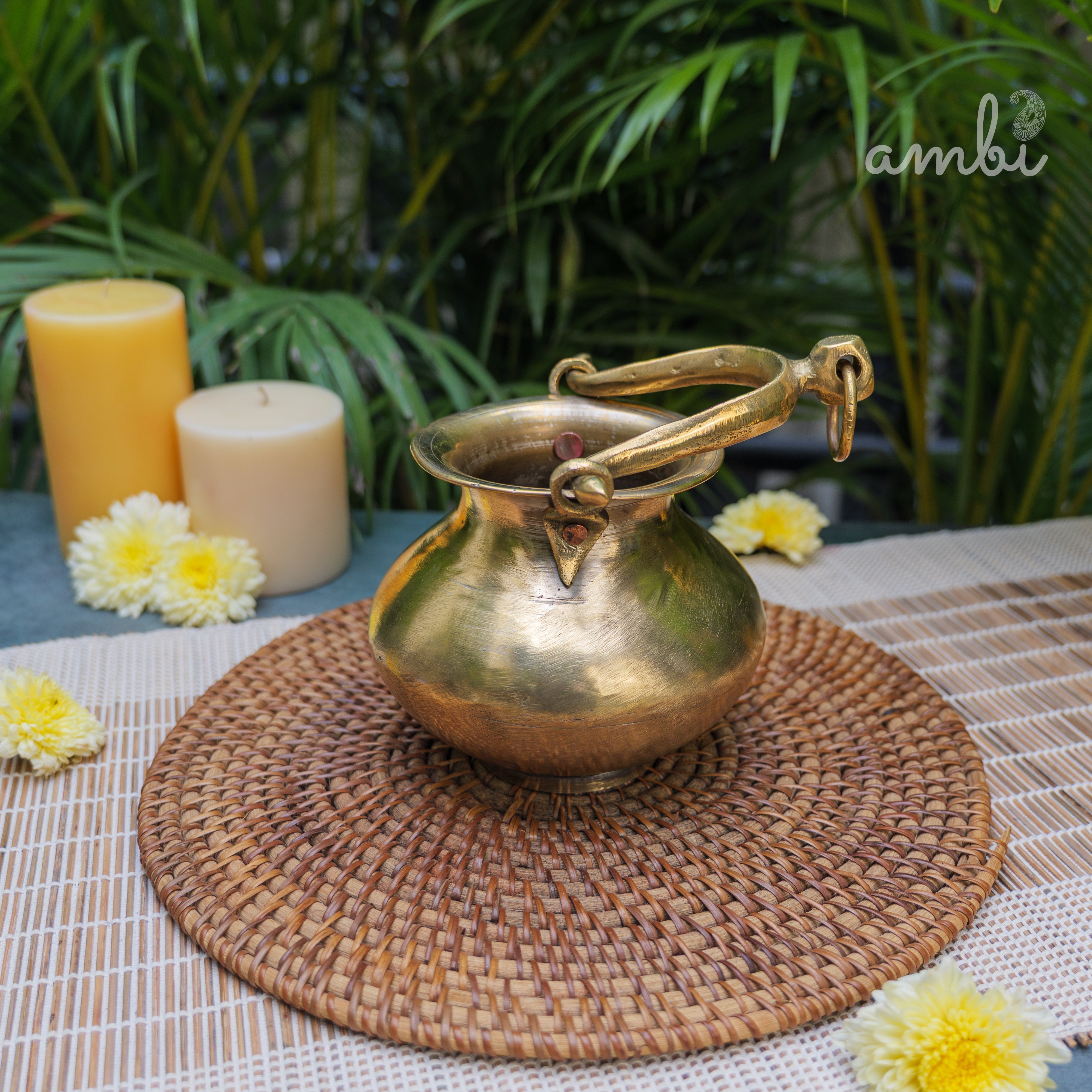 Bronze pot on a woven mat with candles and flowers in the background