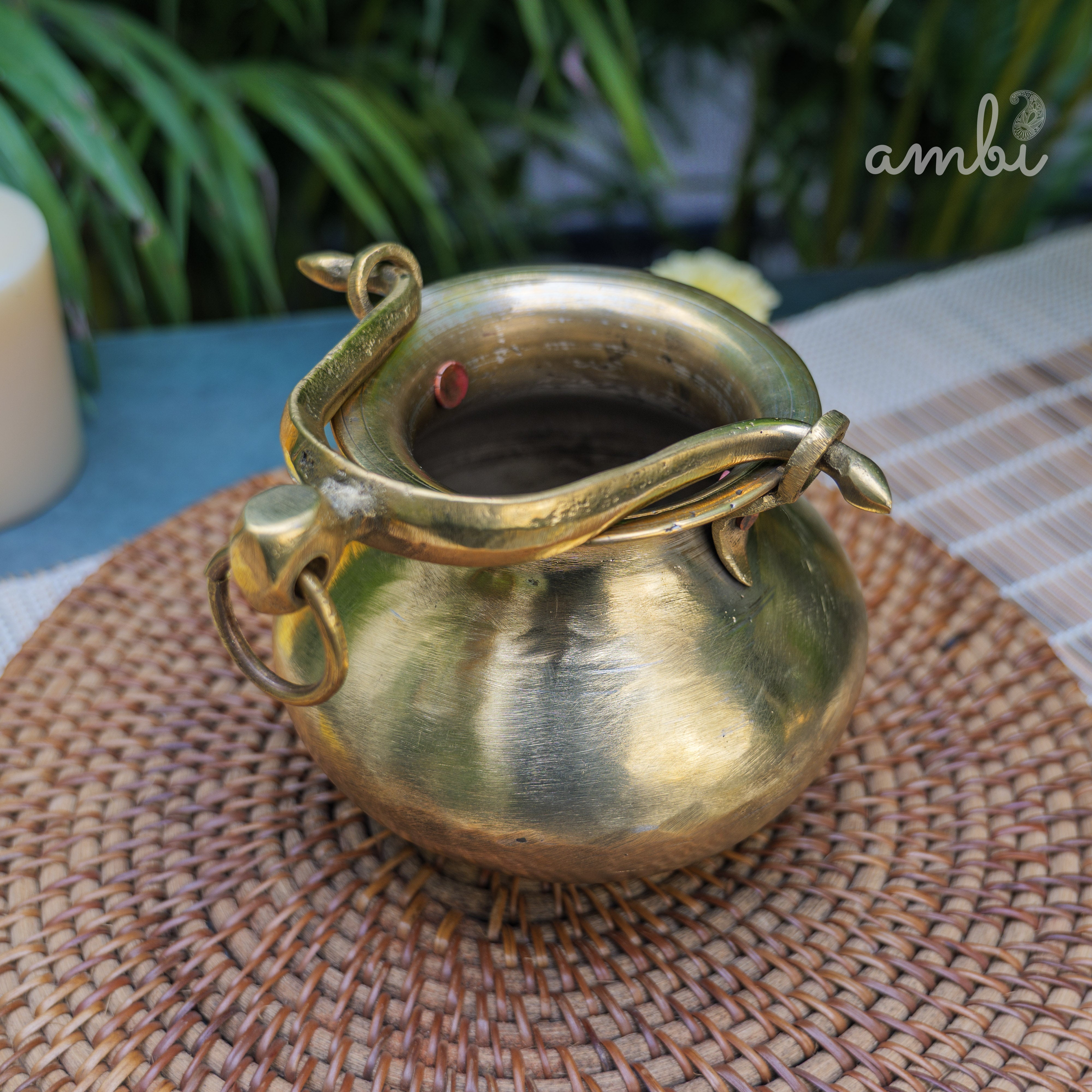 Brass pot with snake design on a woven mat, brand 'ambi' visible