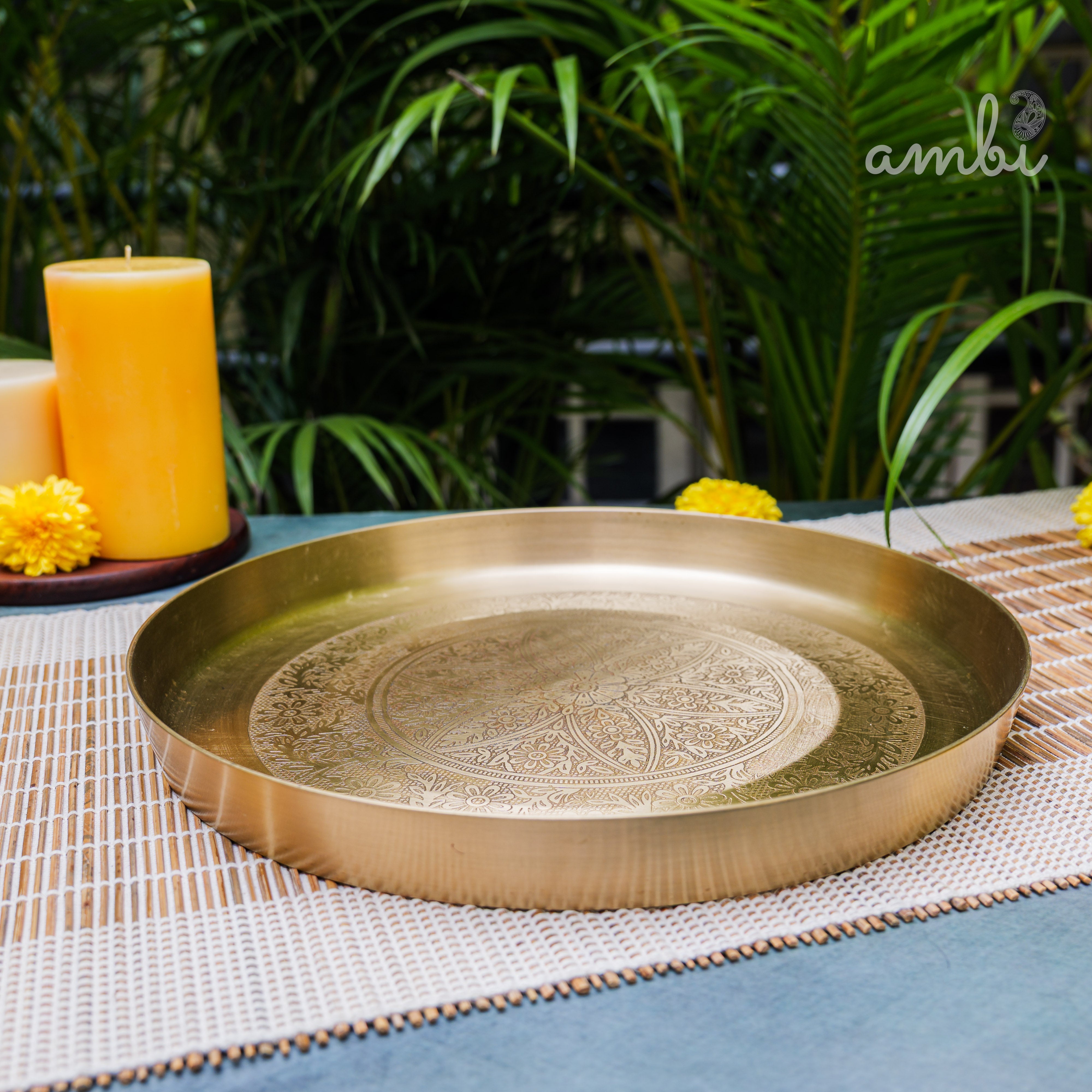 Decorative brass tray on a table with plants and candles in the background