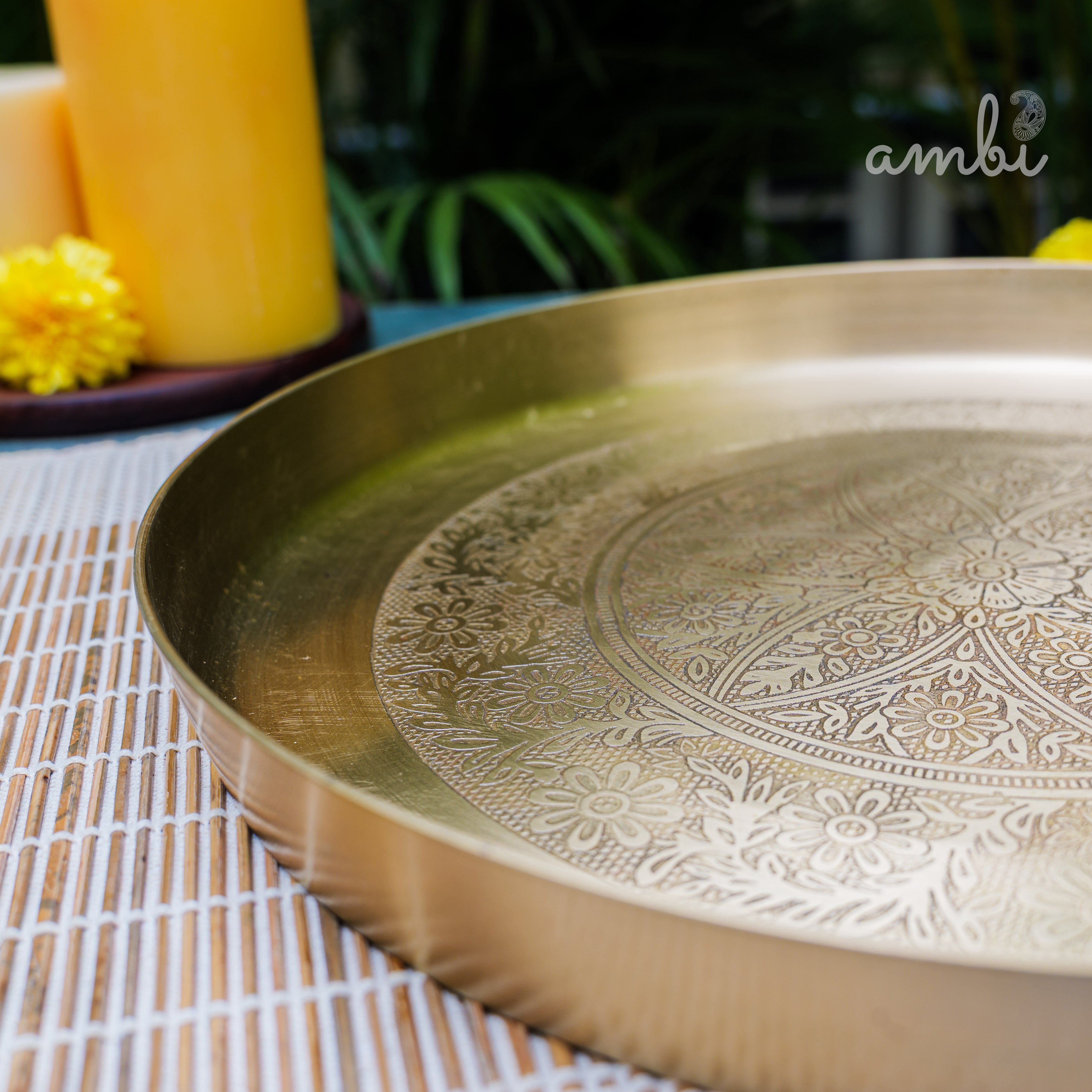 Decorative gold tray with intricate patterns on a tablecloth, featuring the 'ambi' brand.