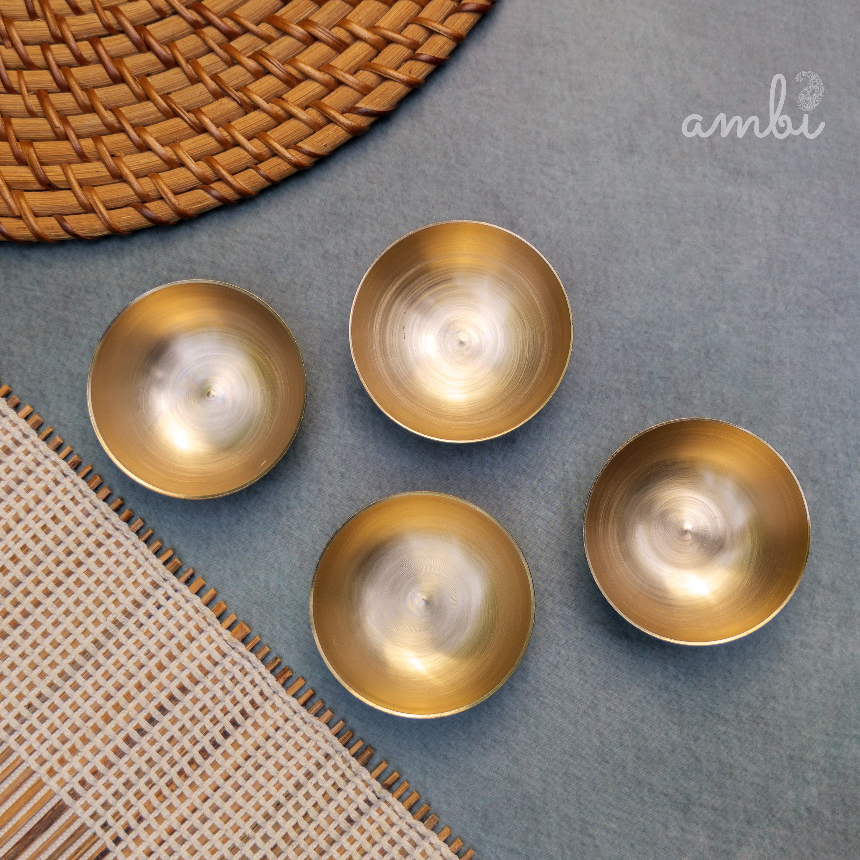 Four gold candle holders with candles on a textured surface, featuring the 'ambi' brand.
