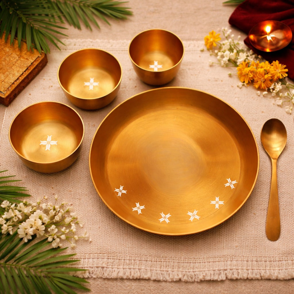 Set of gold ceramic dishes with floral designs on a textured surface with candles and flowers.