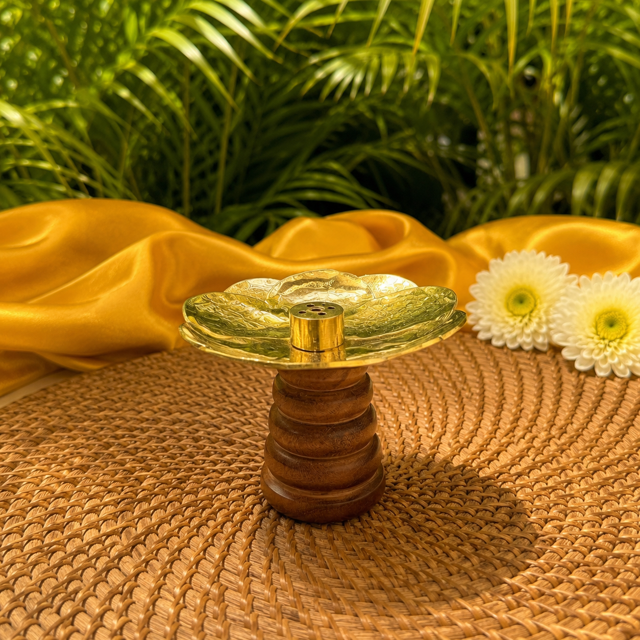 A small decorative candle holder with a translucent green glass flower-shaped top and a ribbed brown wooden base, styled on a woven mat with yellow fabric and white flowers in the background.