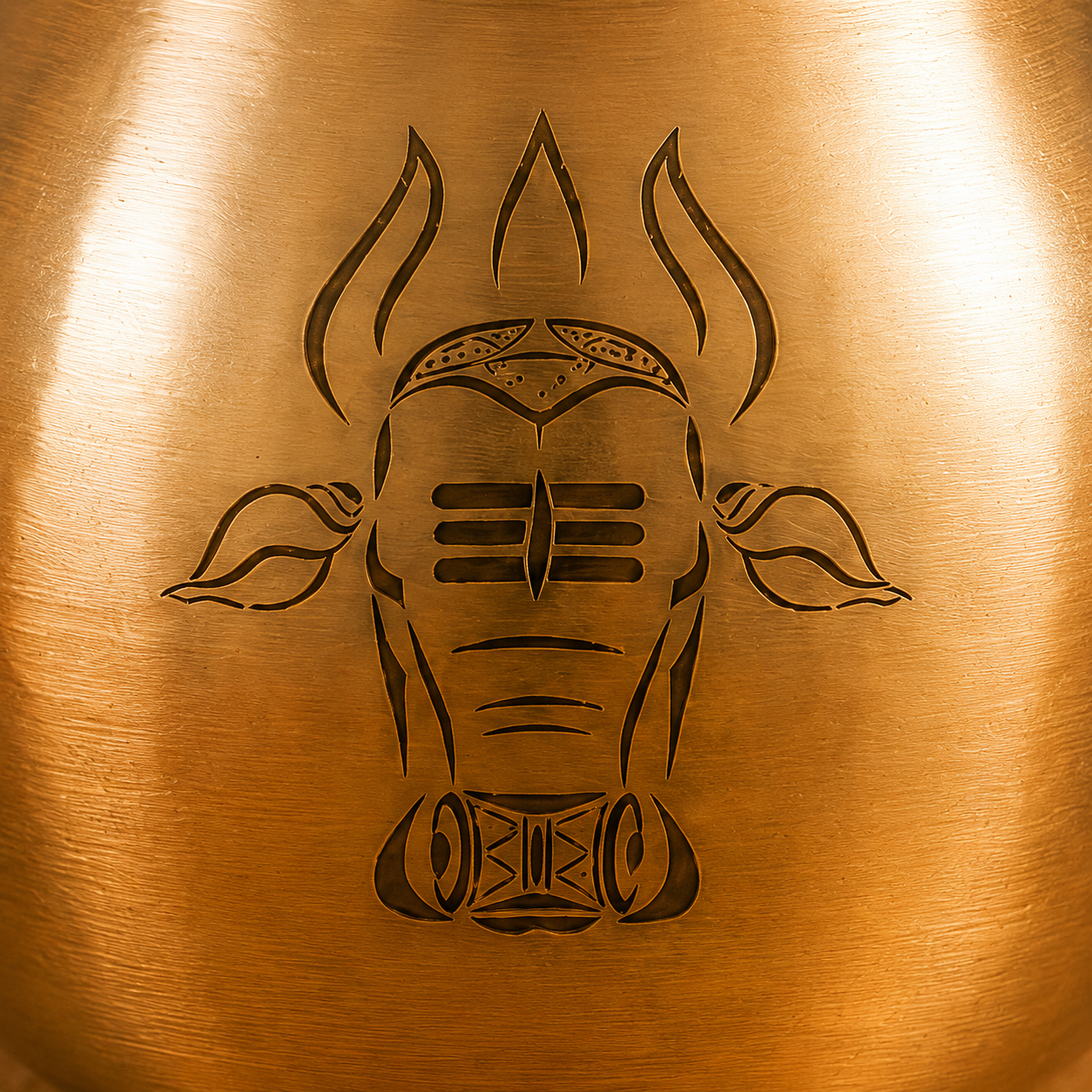 Close-up of a brushed metallic bronze surface with a black stylized Nandi engraving centered on it.