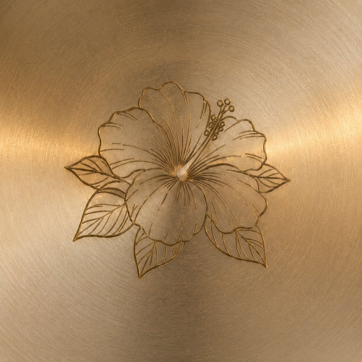 Close-up of a brushed metallic surface with an engraved floral motif in the center, showing warm gold and bronze tones.