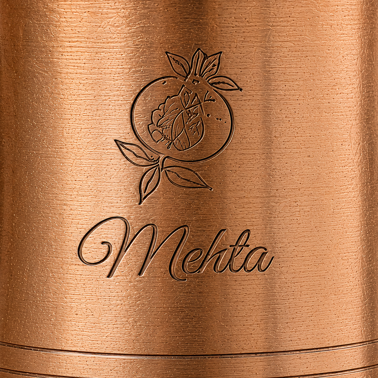 Close-up of a copper-toned metal surface with an engraved citrus illustration and the word 'Mehta' in script.