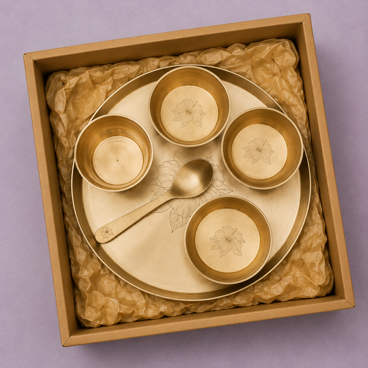 A brass Indian tea or coffee set including a large plate, four small cups, and a spoon, presented in a square gift box lined with brown tissue paper on a purple background.